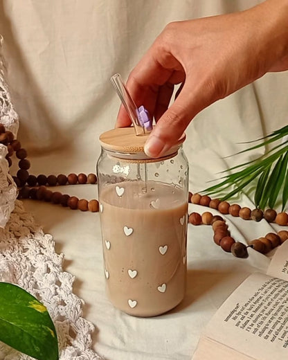 Hand opening a glass jar with a wooden lid on a soft surface with a book and greenery.